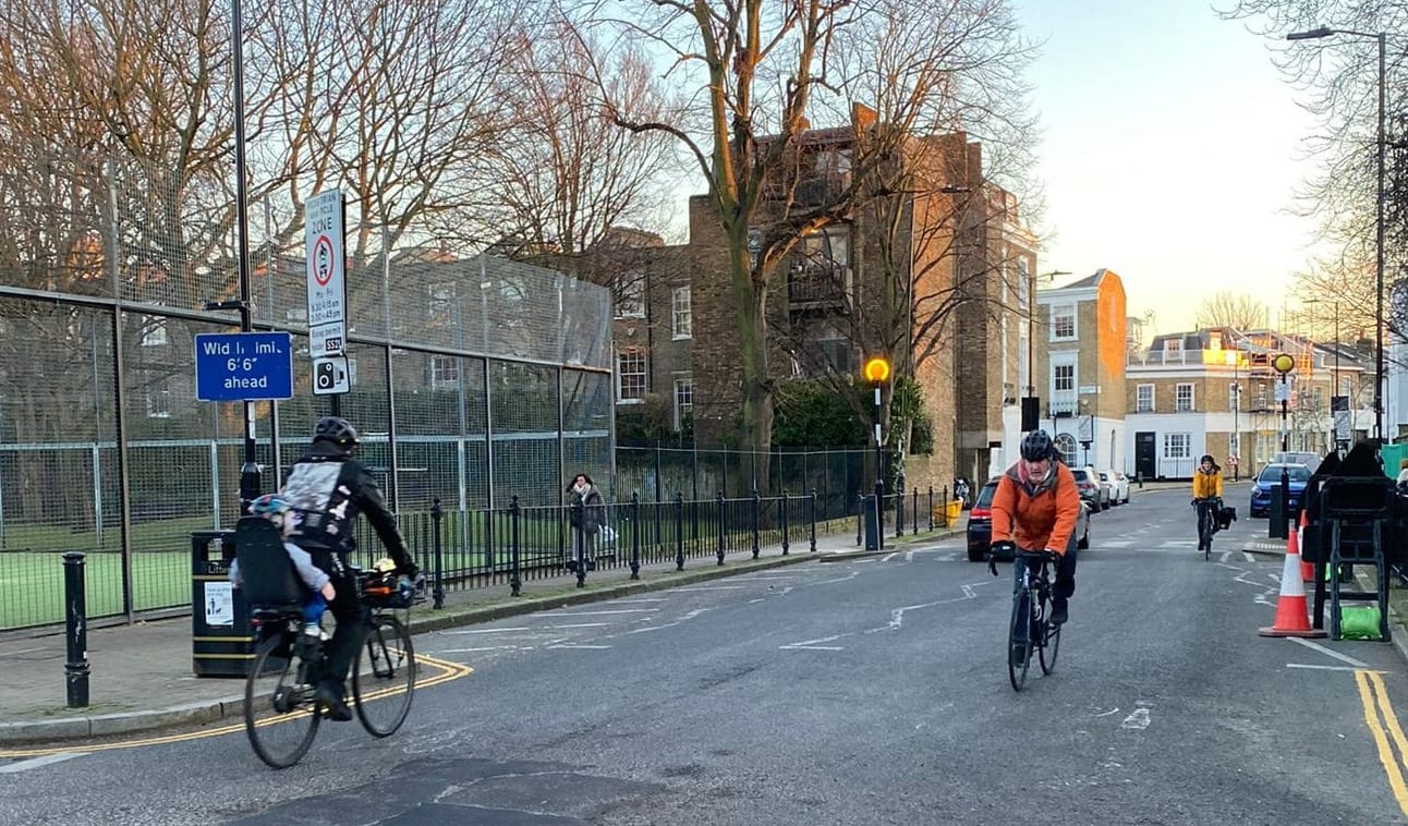 Cyclists pass Thornhill school. One of them has a child in a bike seat on the back.