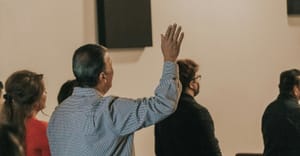 People stand in a room, and one man raises his hand.